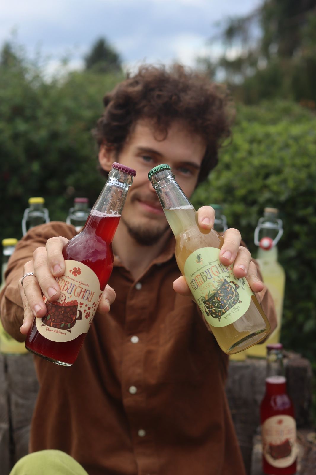 Désiré tend deux bouteilles de 33 cl, hibiscus et sauge-thym